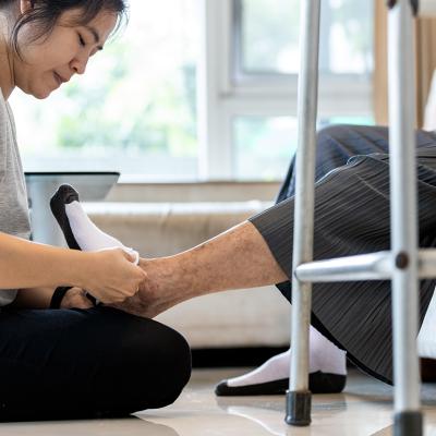 A female caregiver helping a senior person to wear socks at home.