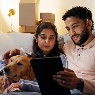 A couple with their dog relaxing in their new home and watching from a tablet.