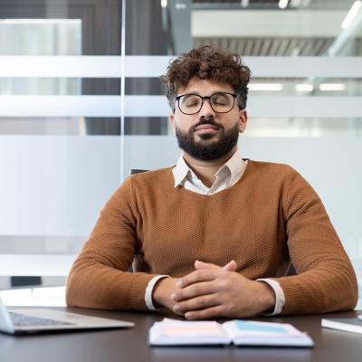 A man with eyes closed meditating at his office desk.