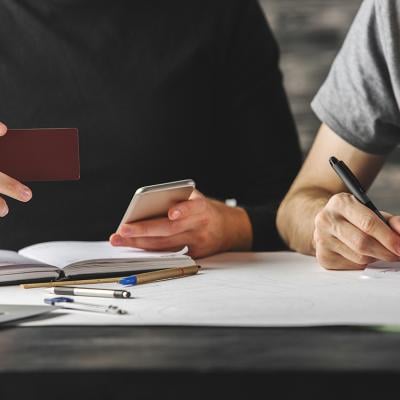 Young man holding credit card beside another person writing down information.