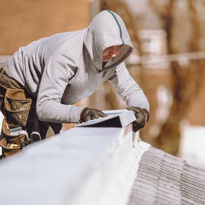 A repairman putting a metal ridge on top of a roof.