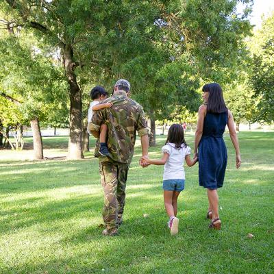 Back view of happy family walking together in a park. The father is wearing camouflage military uniform.