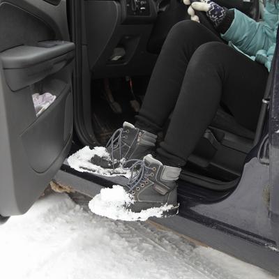 A young woman shaking snow off her boots while getting out of a car.