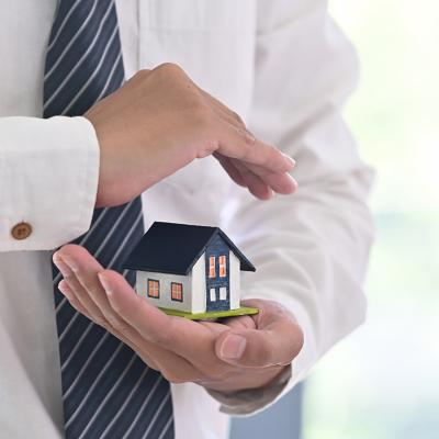 A real estate agent holding a small figure of a house in a protective gesture as a concept of insurance.