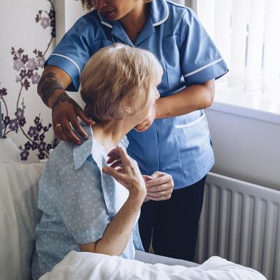 A home caregiver helping a senior woman get dressed in bed.