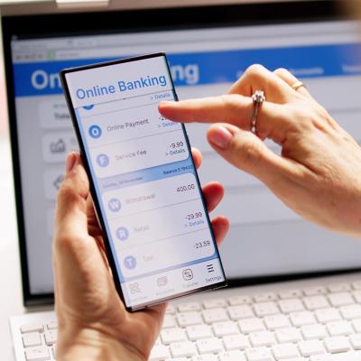 Person using online banking on a smartphone and laptop.