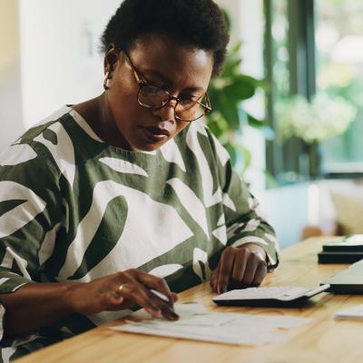 A black woman reviewing and calculating financial reports at home.