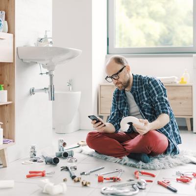 A man watching something on his smartphone while repairing a sink at home.
