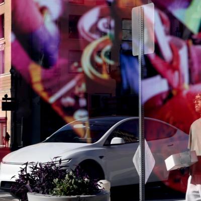 A Tesla car and pedestrians caught in a reflection on a storefront window.