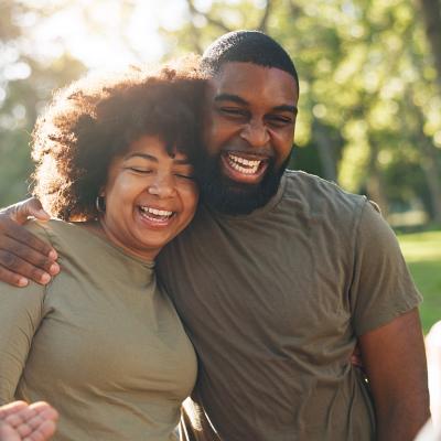 A happy Black couple hug and laugh outdoors.