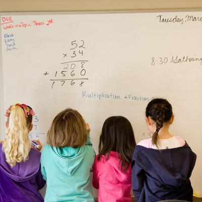 A group of children working to solve math problems on a whiteboard.