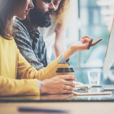 A group of coworkers pointing at a computer monitor while accessing the internet in their office.