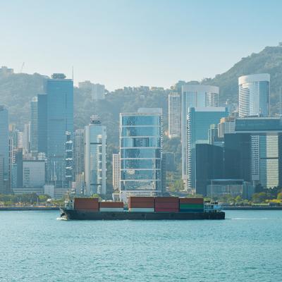 A cargo ship on the Victoria Harbour with the Hong Kong skyline in the background.