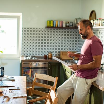 A man reading a utility bill in the kitchen at home.