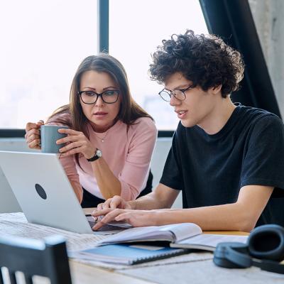 A mother and her Gen Z son looking at a laptop together at home.