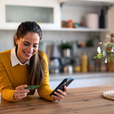 A woman using a smartphone, holding a credit card, while also checking an online bank account.