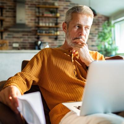 A man thinking with a laptop on his lap at home. 