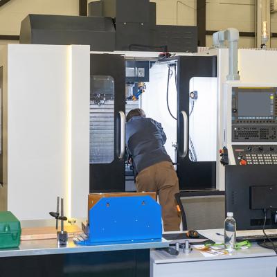 A man looking inside a CNC machine during a maintenance process in a production workshop.