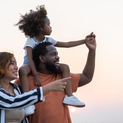 A portrait of a happy family with the daughter being carried by the father on his shoulders.