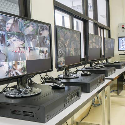 A security room with a row of monitors displaying multiple CCTV footage areas.