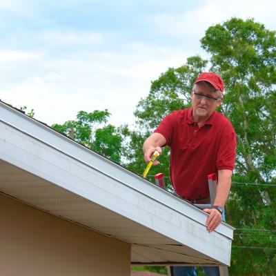 A wind mitigation inspector on a ladder doing inspection on a homeowner's new roof.