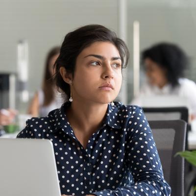 An employee looking away from a laptop in the office. 