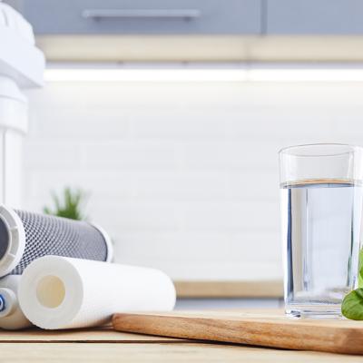 A glass of clean filtered water beside replacement filters of an osmosis water filtration system.