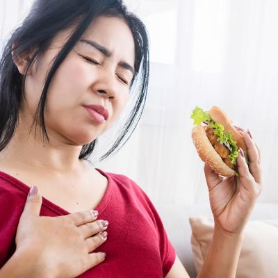 A person experiencing a heartburn while eating a burger.