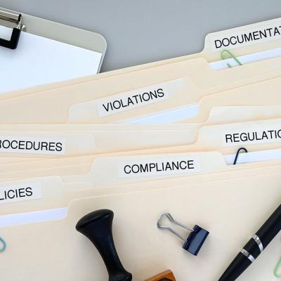Folders of compliance and policy documents on a desk.