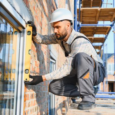 A construction worker installing a window while standing on scaffolding.