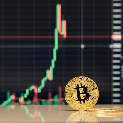 A golden bitcoin in front of stock exchange charts.