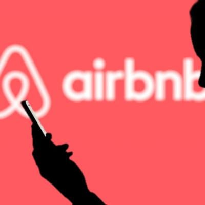 Silhouette of a man using a phone against a background showing Airbnb's logo.