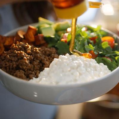 Honey poured onto a bowl of chili, cottage cheese, and salad dish for a protein-rich source meal.