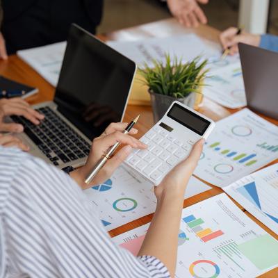 Businesswoman using a calculator while reviewing reports.