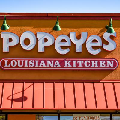 orizontal, medium closeup of "Popeyes" Louisiana Kitchen exterior facade brand and logo signage in white letters on a bright sunny day.