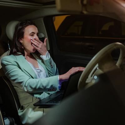 An employee yawning inside her car after work. 