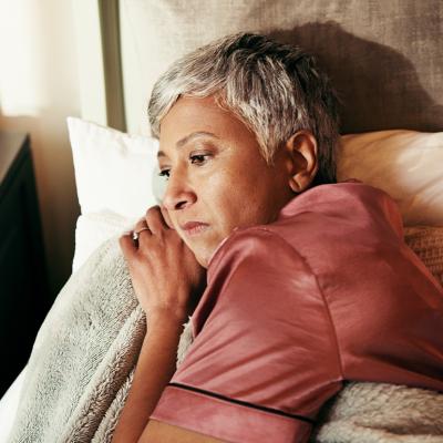 A middle-aged woman lying in bed in deep thought.