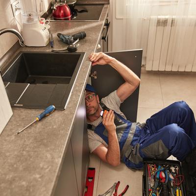 A plumber fixing a water pipe under the kitchen sink. 