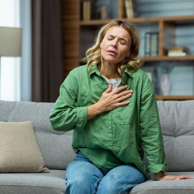 A woman sitting on a sofa holding her chest due to pain.