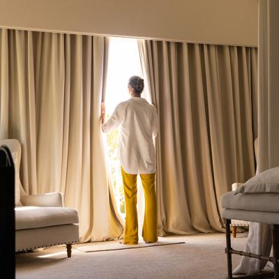 A senior woman standing by the large window of a cozy living room.