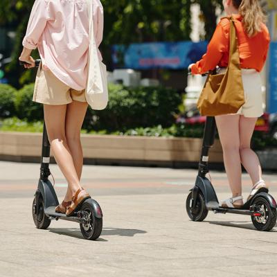 Two women riding electric scooters outdoors.