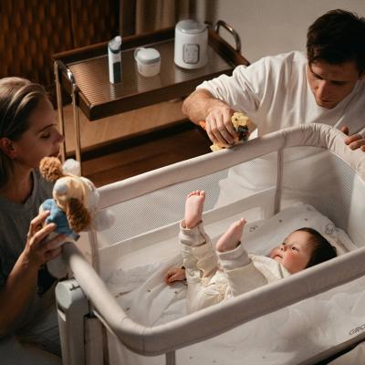 Parents entertaining their baby in a crib with toys.