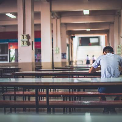 A male high school student sitting alone at a cafeteria.