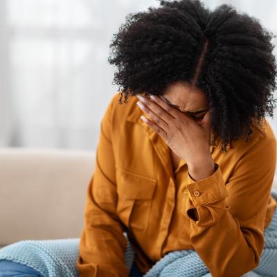 A young black woman sitting on a sofa holding her due to stress.
