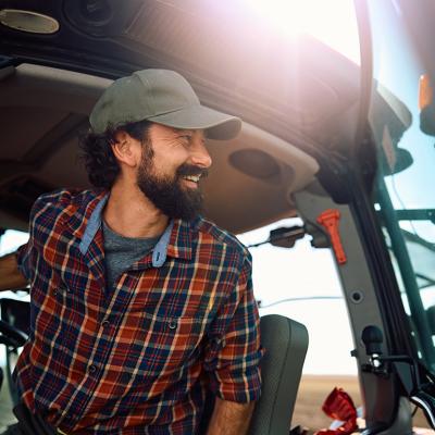 A farm worker in a tractor looking at an agricultural field.