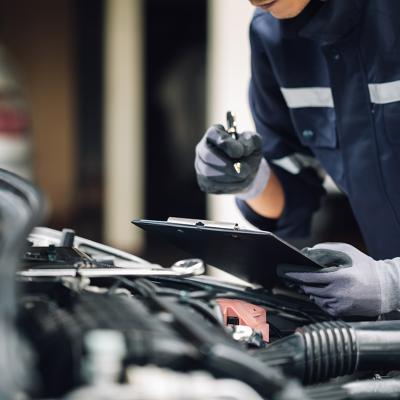 A car mechanic doing a checklist while looking at an engine.