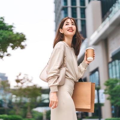 A young woman holding a cup of coffee and shopping bag outdoors.