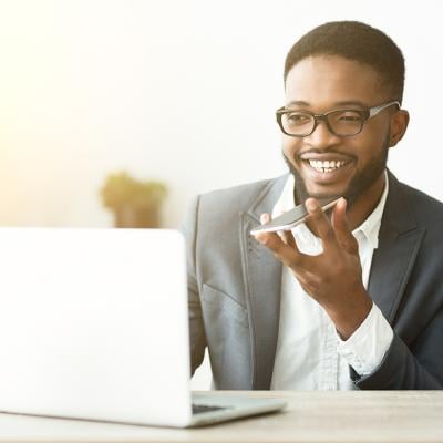 A happy young black businessman using voice assistant on his smartphone.