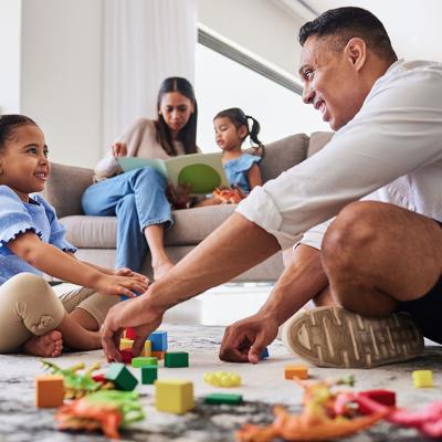 Parents playing with and reading a book to their young daughters at home.