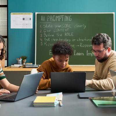 A male teacher guiding students in a classroom in using AI.